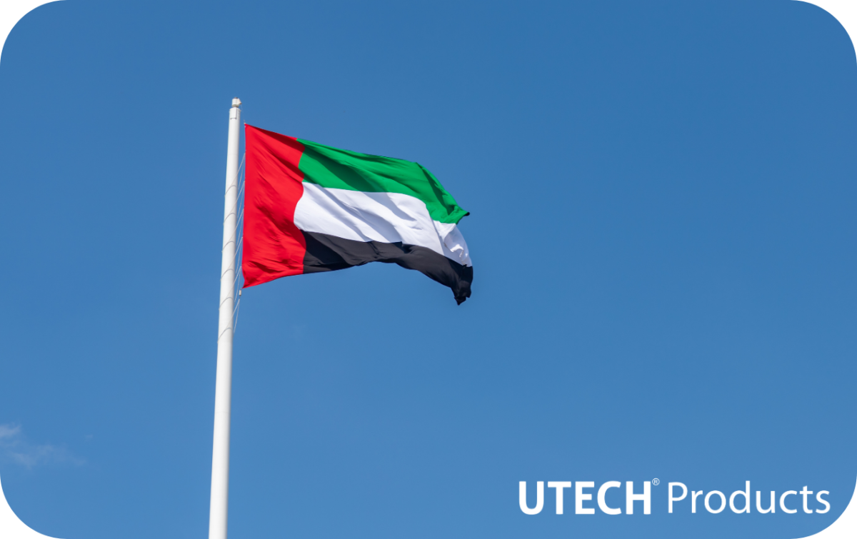 A clear, blue sky with a United Arab Emirates flag flying on a traditional flagpole. An all-white version of the Utech Products logo is in the bottom right corner.