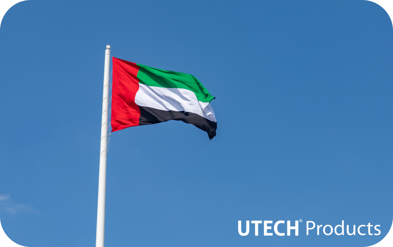A clear, blue sky with a United Arab Emirates flag flying on a traditional flagpole. An all-white version of the Utech Products logo is in the bottom right corner.